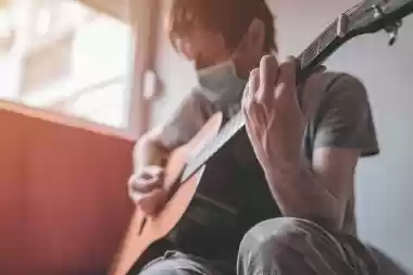Musician wearing a face mask playing guitar at home during Covid-19