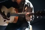 Guitarist playing acoustic guitar in a dark setting
