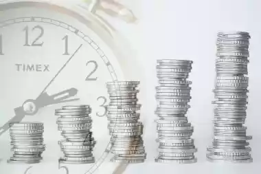Stacks of coins growing in height in front of a clock, representing pension savings over time