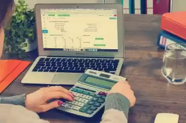 Person using a calculator with a laptop showing a tax spreadsheet
