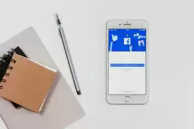 Smartphone showing Facebook login screen next to notebooks and pen