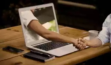 Hand reaching through a laptop screen for a handshake representing online networking